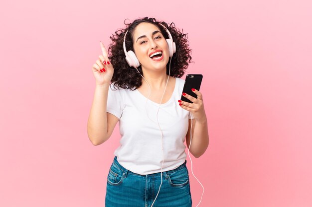 Bonita mujer árabe que se siente como un genio feliz y emocionado después de realizar una idea con auriculares y un teléfono inteligente.