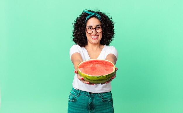 Bonita mujer árabe sonriendo alegremente con amabilidad y ofreciendo y mostrando un concepto y sosteniendo una sandía. concepto de verano