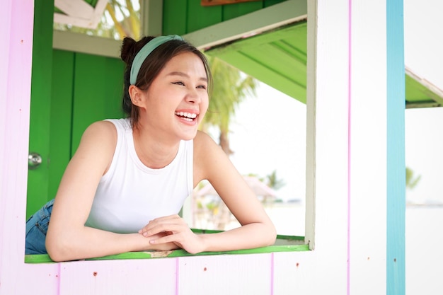 Bonita mujer asiática sonriendo feliz dentro de una casa de madera de juguete En la playa junto al concepto de viaje por mar