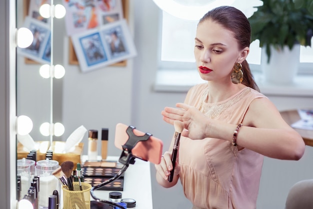 Bonita mujer bonita dando consejos sobre el pincel de maquillaje mientras tiene su propio blog