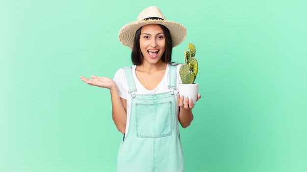 Bonita mujer campesina que se siente feliz y asombrada por algo increíble y sostiene un cactus