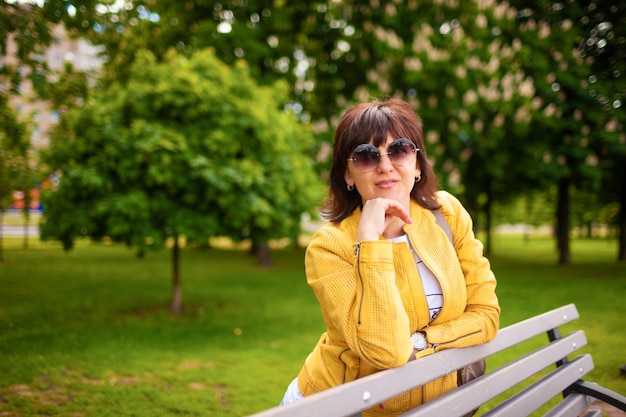 Bonita mujer caucásica atractiva pelirroja en ropa casual y gafas de sol posando en un banco del parque en un día soleado de primavera