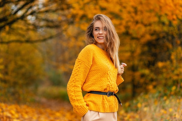 Bonita mujer caucásica feliz con dulce sonrisa en suéter de punto vintage descansar y disfrutar en el parque con follaje amarillo otoñal. Estilo de color femenino y belleza de otoño.