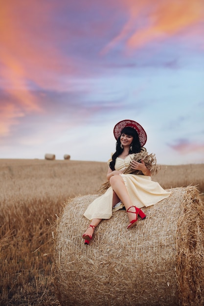 Bonita mujer caucásica con largo cabello negro ondulado en vestido amarillo largo y sombrero rojo se sienta y se relaja