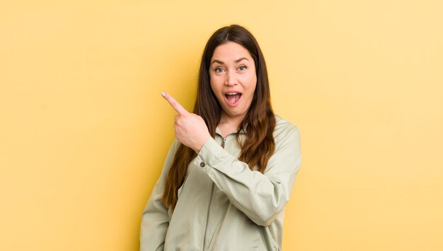 Bonita mujer caucásica mirando emocionado y sorprendido apuntando hacia un lado y hacia arriba para copiar el espacio