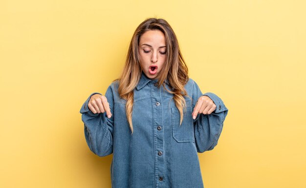 bonita mujer caucásica que se siente sorprendida, con la boca abierta y asombrada, mirando y apuntando hacia abajo con incredulidad y sorpresa