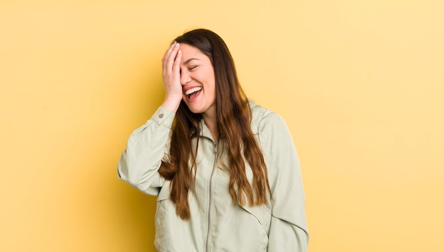 Bonita mujer caucásica riéndose y golpeándose la frente como diciendo d'oh, lo olvidé o eso fue un error estúpido