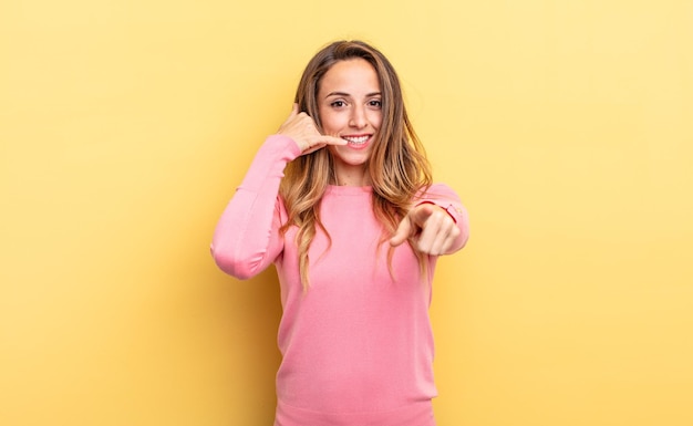 Foto bonita mujer caucásica sonriendo alegremente y apuntando a la cámara mientras hace una llamada, gesto más tarde, hablando por teléfono