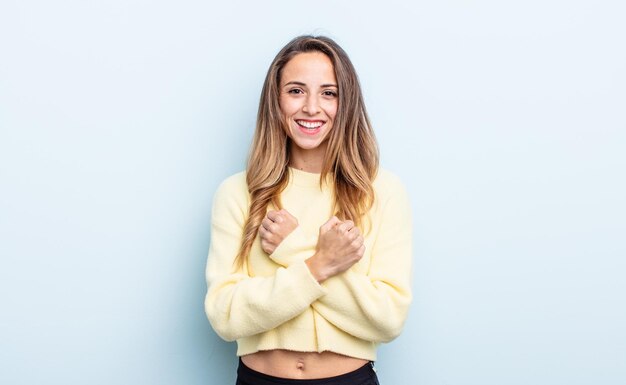 Bonita mujer caucásica sonriendo alegremente y celebrando, con los puños apretados y los brazos cruzados, sintiéndose feliz y positiva