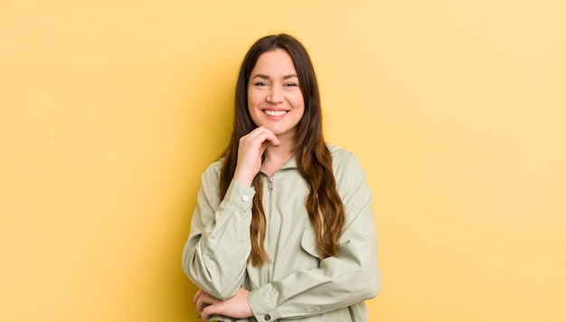 Bonita mujer caucásica sonriendo disfrutando de la vida sintiéndose feliz amistosa satisfecha y despreocupada con la mano en la barbilla