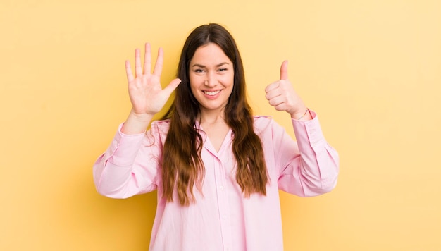 Bonita mujer caucásica sonriendo y luciendo amigable mostrando el número seis o sexto con la mano hacia adelante contando hacia atrás