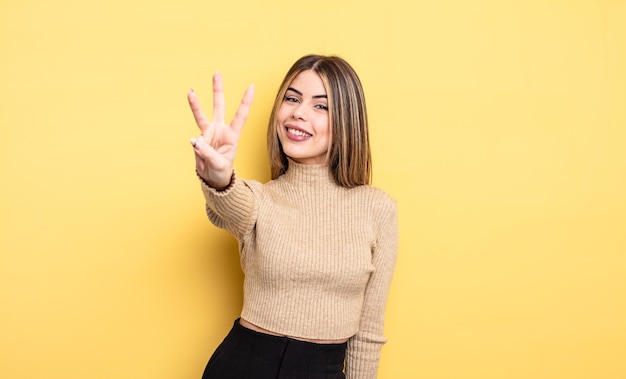 Bonita mujer caucásica sonriendo y mirando amistosamente, mostrando el número tres o tercero con la mano hacia adelante, contando hacia atrás