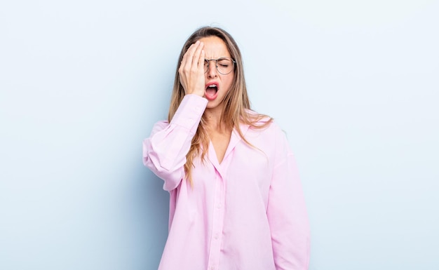 bonita mujer caucásica con sueño, aburrida y bostezando, con dolor de cabeza y una mano cubriendo la mitad de la cara