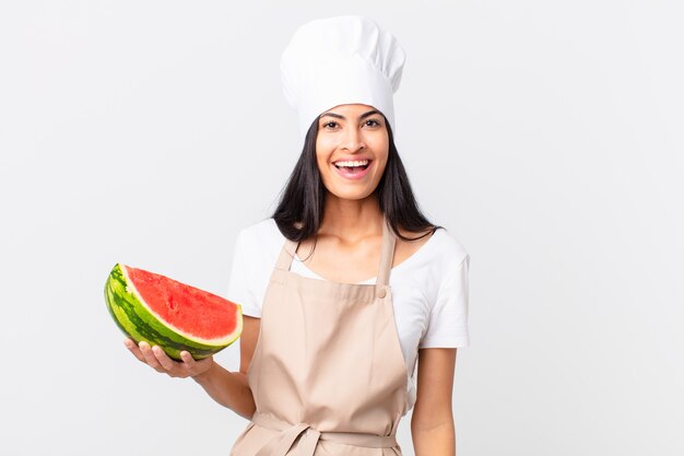 Bonita mujer chef hispana mirando feliz y gratamente sorprendido y sosteniendo una sandía