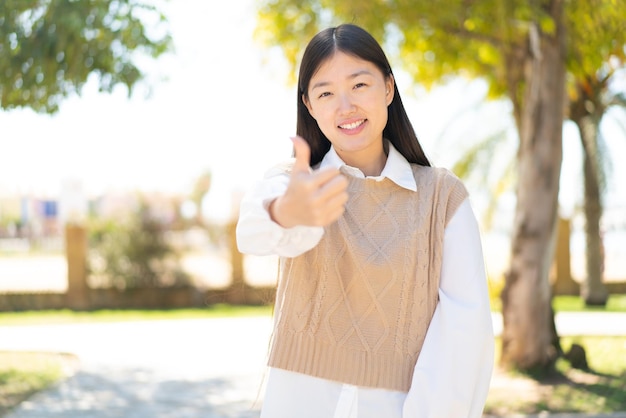 Bonita mujer china al aire libre con los pulgares hacia arriba porque ha sucedido algo bueno