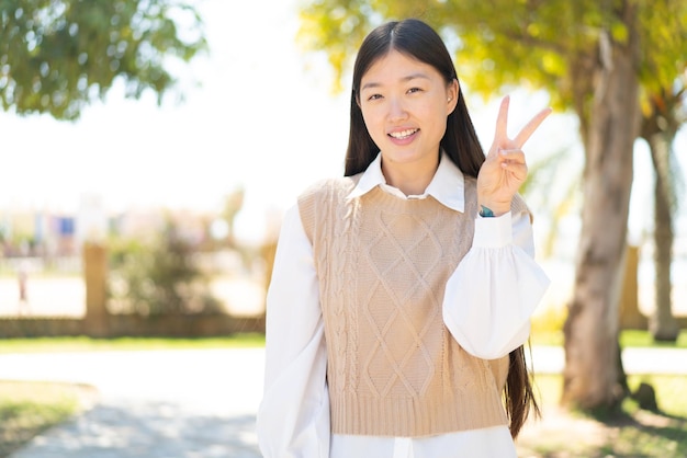 Bonita mujer china al aire libre sonriendo y mostrando el signo de la victoria