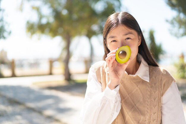 Bonita mujer china al aire libre sosteniendo un aguacate