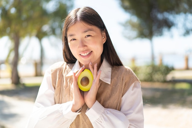 Bonita mujer china al aire libre sosteniendo un aguacate