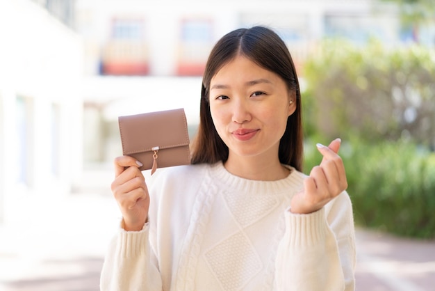 Bonita mujer china al aire libre sosteniendo billetera con gesto de dinero