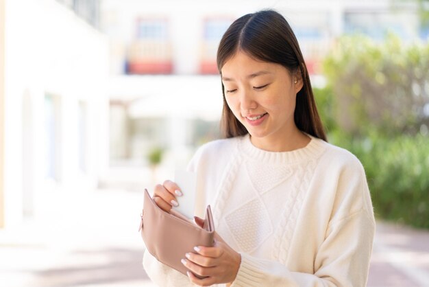 Bonita mujer china al aire libre sosteniendo billetera y tarjeta de crédito con expresión feliz