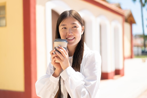 Bonita mujer china al aire libre sosteniendo un café para llevar y teniendo dudas