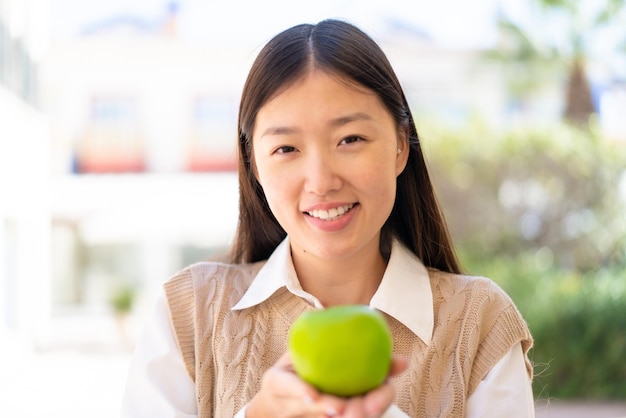 Bonita mujer china al aire libre sosteniendo una manzana con expresión feliz