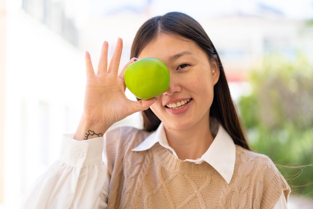 Bonita mujer china al aire libre sosteniendo una manzana con expresión feliz