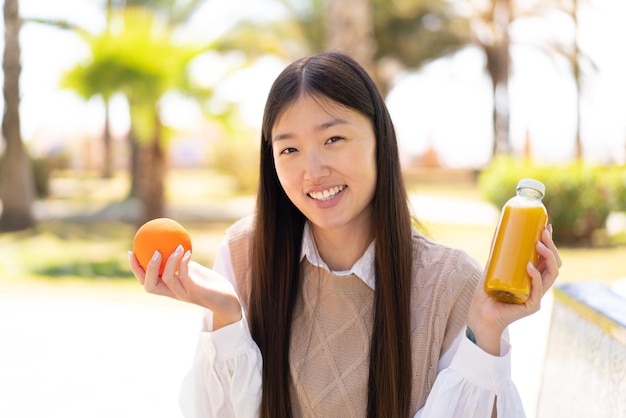 Bonita mujer china al aire libre sosteniendo una naranja y un jugo de naranja