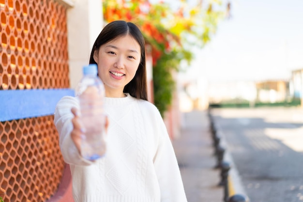 Bonita mujer china con una botella de agua al aire libre con expresión feliz