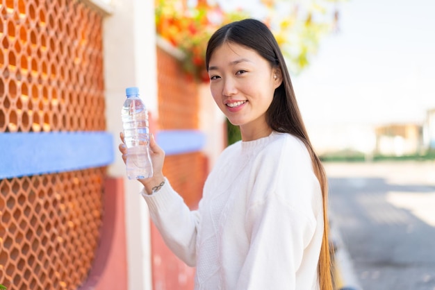 Bonita mujer china con una botella de agua al aire libre sonriendo mucho