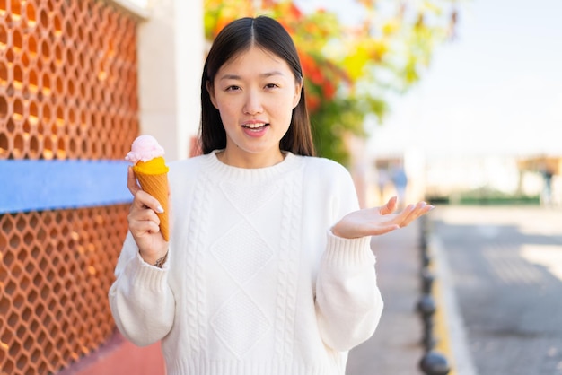 Bonita mujer china con un helado de cucurucho al aire libre con una expresión facial conmocionada