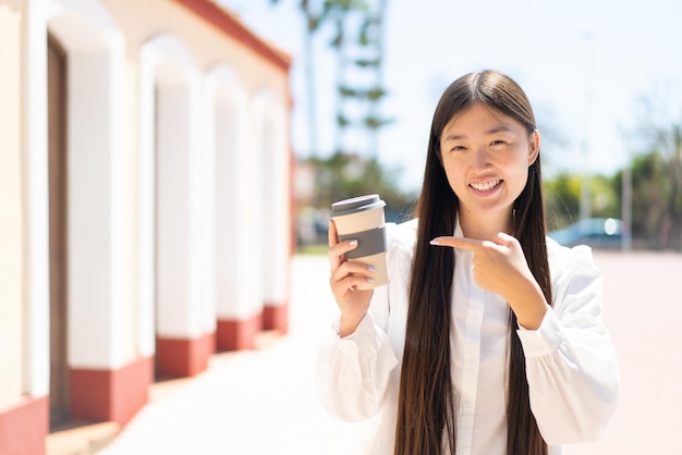 Bonita mujer china sosteniendo un café para llevar al aire libre y apuntándolo