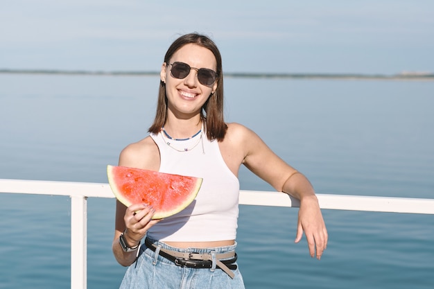 Bonita mujer con gafas de sol sosteniendo una gran rebanada de sandía