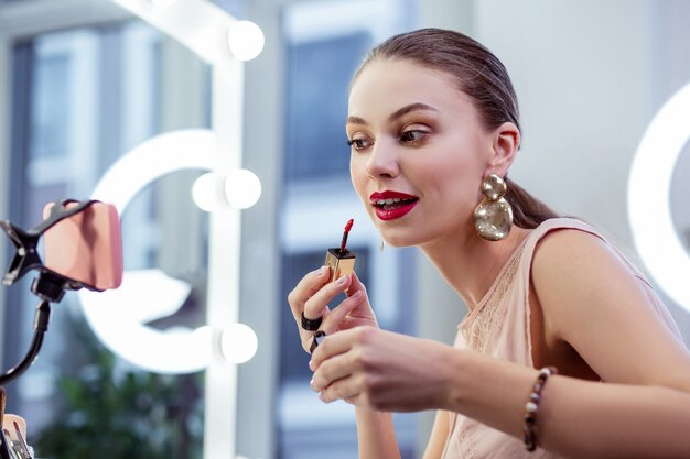 Bonita mujer guapa sentada frente a la cámara mientras aplica lápiz labial rojo