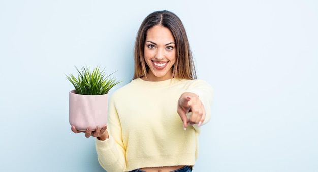 Bonita mujer hispana apuntando a la cámara eligiéndote. concepto de planta de interior