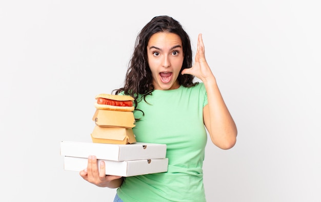 Bonita mujer hispana gritando con las manos en el aire y sosteniendo cajas de comida rápida para llevar