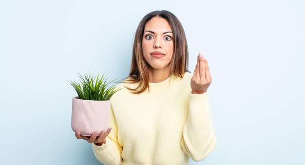 Bonita mujer hispana haciendo capice o gesto de dinero, diciéndote que pagues. concepto de planta de interior