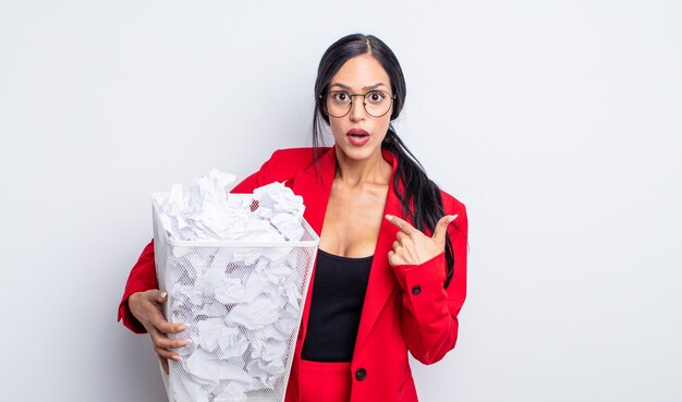 Bonita mujer hispana mirando conmocionado y sorprendido con la boca abierta, apuntando al concepto de basura de bolas de papel auto