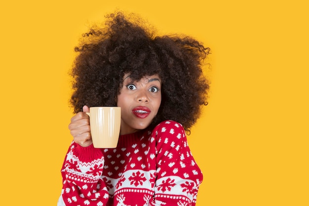 Bonita mujer hispana de navidad latina, con una taza de café, cara de sorpresa, fondo amarillo