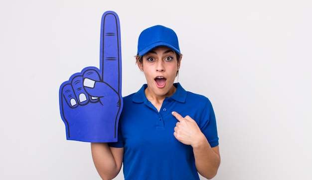 Bonita mujer hispana que parece conmocionada y sorprendida con la boca abierta apuntando a la mano del ventilador número uno