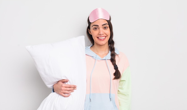 Bonita mujer hispana que parece feliz y gratamente sorprendida con el concepto de pijama y almohada