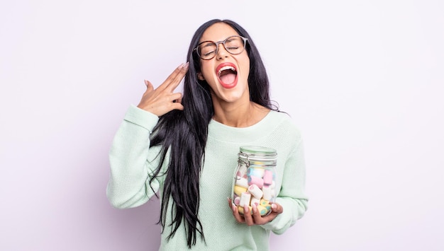 Bonita mujer hispana que parece infeliz y estresada, gesto de suicidio haciendo signo de pistola concepto de caramelos de gelatina