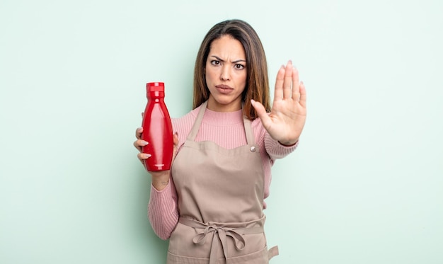 Bonita mujer hispana que parece seria mostrando la palma abierta haciendo un gesto de parada. concepto de salsa de tomate