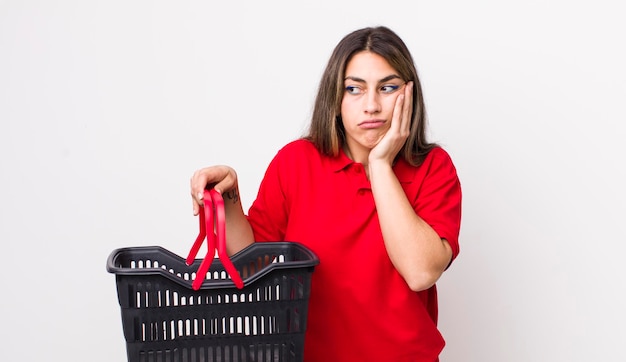 Bonita mujer hispana que se siente aburrida, frustrada y con sueño después de un aburrido concepto de cesta de la compra vacía