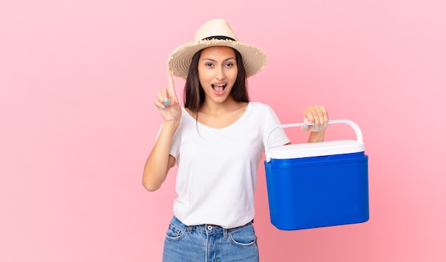 Bonita mujer hispana que se siente como un genio feliz y emocionado después de darse cuenta de una idea y sostener un refrigerador portátil