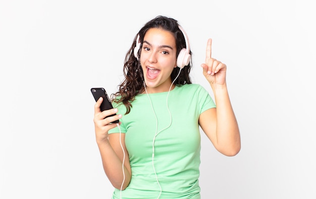 Bonita mujer hispana que se siente como un genio feliz y emocionado después de realizar una idea con auriculares y un teléfono inteligente.