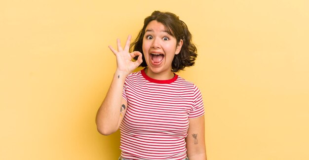 Bonita mujer hispana que se siente exitosa y satisfecha sonriendo con la boca abierta haciendo un buen signo con la mano