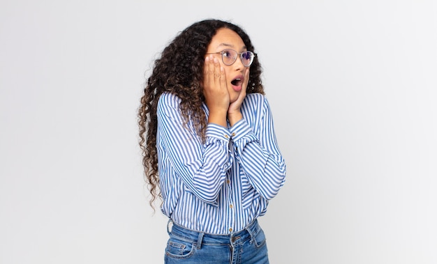 Bonita mujer hispana que se siente feliz, emocionada y sorprendida, mirando hacia el lado con ambas manos en la cara