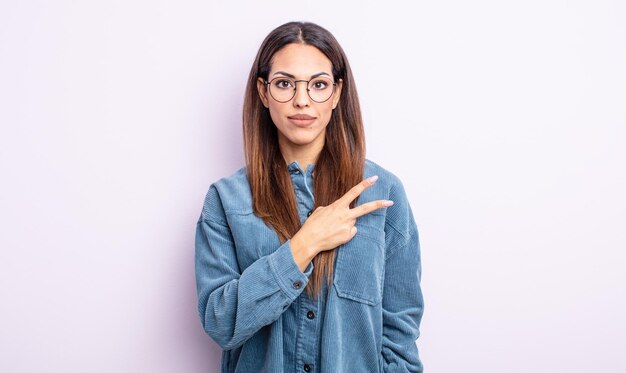 Bonita mujer hispana que se siente feliz, positiva y exitosa, con la mano haciendo forma de v sobre el pecho, mostrando la victoria o la paz