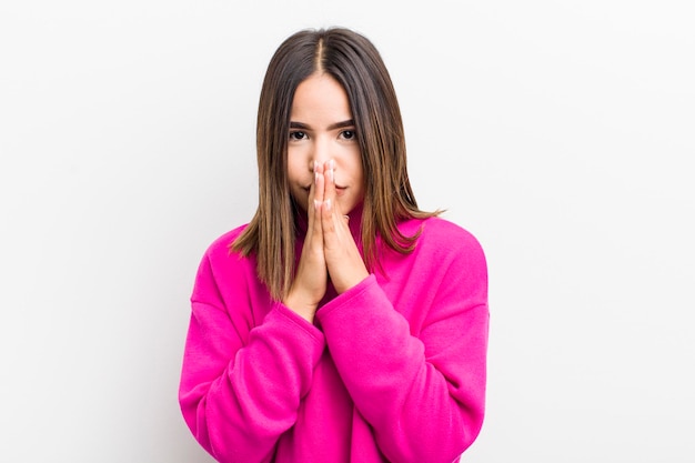 Bonita mujer hispana que se siente preocupada, esperanzada y religiosa, orando fielmente con las palmas presionadas pidiendo perdón